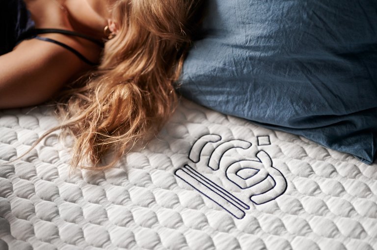 Afbeelding van een deel van het hoofd op een kussen en de schouder van een vrouw op een matras ligt met daarnaast ingenaaide Auping Evolve logo van het bedrijf Auping