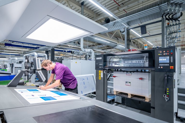 Beeld van de drukkerij van Veldhuis Media waarop een drukker drukvellen beoordeelt aan een offset drukpers.